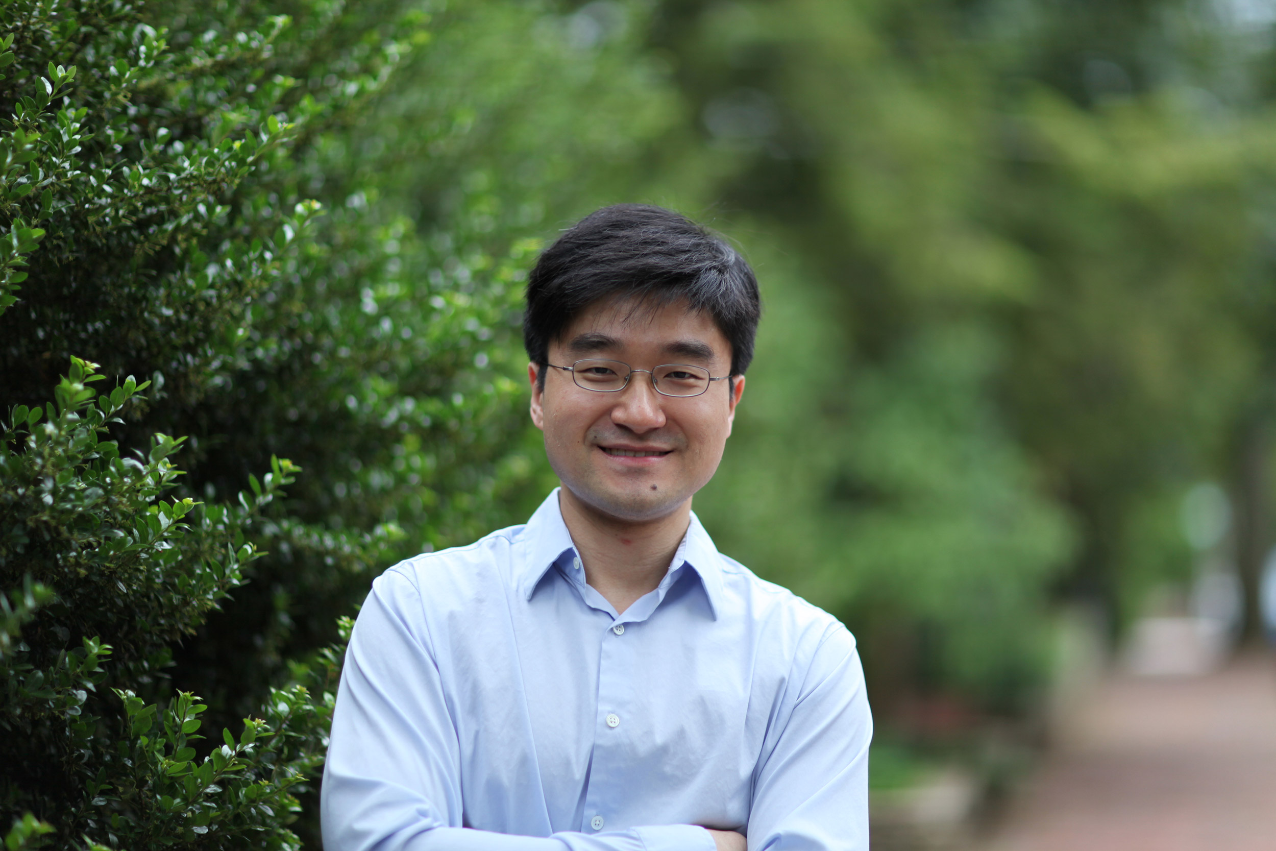 A photo of Xin Li standing in front of hedges