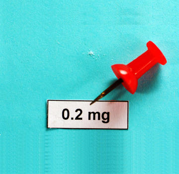 A few crystals of powder lie next to a bright red pin. The collected powder is barely enough to cover the tip of the pin.