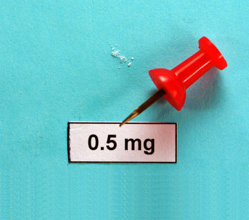 A pinch of crystals lies next to a bright red pin. The powder could fit on a dime.