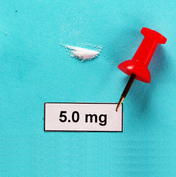 A small pile of powder, no larger than the head of the pin, lies next to a bright red pin