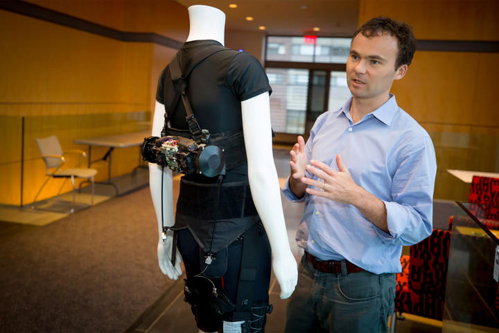A photo of Conor Walsh standing with one of his robotic designs
