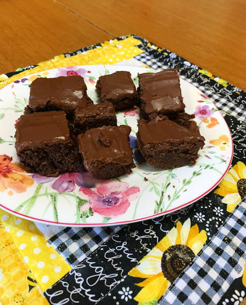 A photo of a plate full of brownies with chocolate icing on top