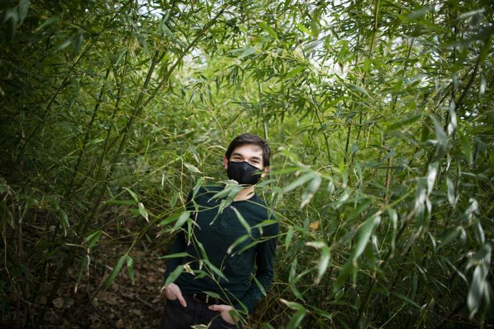 A photo of Noah Secondo outdoors, surrounded by tall green plants