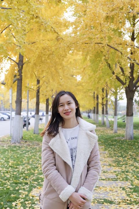 A photo of Cristina Su Liu standing on a sidewalk under trees with yellow leaves