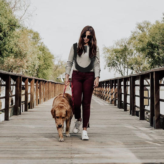 A photo of a blind woman walking with her guide dog and wearing the Foresight navigational aid around her upper body