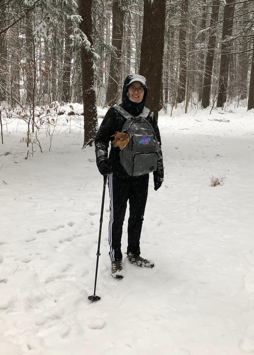 A photo of Hannah Sim on a snowy trail with Louie in her backpack