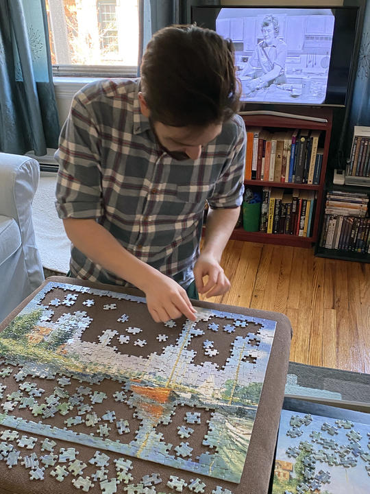 Matt Volpe working on a puzzle with Julia Child on TV in the background