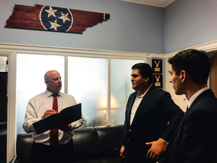 DesJarlais writes in a notebook as he listens to Macuri-Espinoza talk. Above his head are wooden planks cut into the shape of Tennessee with the state's flag--three white stars on a blue circle surrounded in red--painted on them.