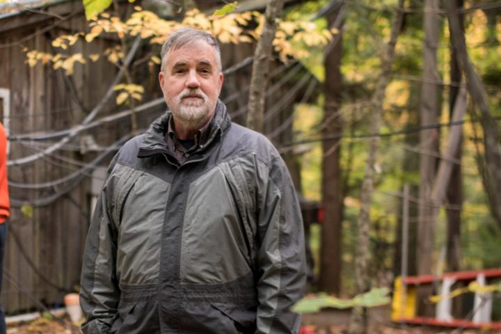 A photo of J. William Munger in a winter jacket in front of trees with yellow leaves