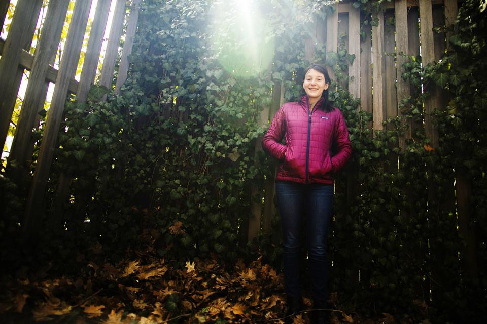 A photo of Libby Dimenstein standing in front of an ivy-covered wooden fence