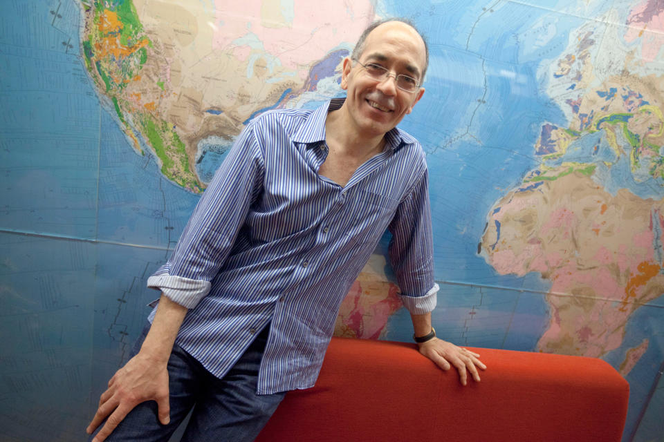 A photo of Jerry Mitrovica in front of a wall-sized map