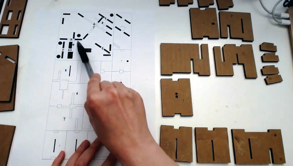 A screenshot of Hsu pointing to a schematic with different sized cardboard rectangles next to it