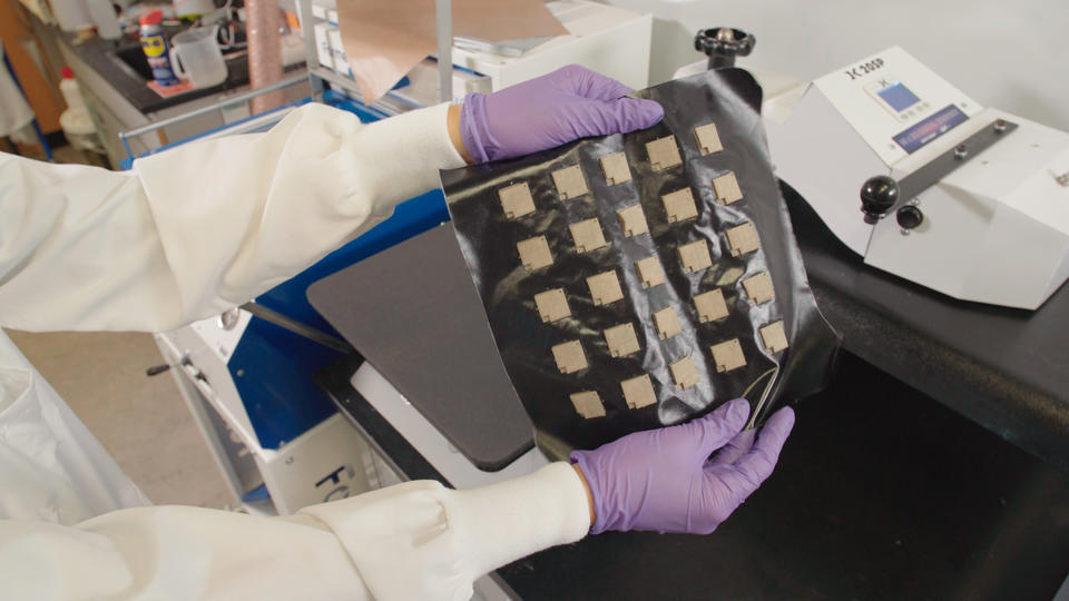 A photo of a lab member holding a square of the Smart Thermally Actuating Textiles with embedded sensors