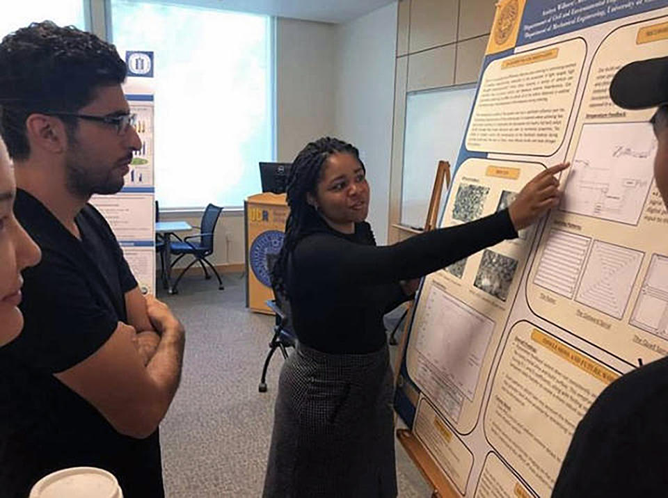 A photo of Milan Wilson presenting a poster to a group of onlookers